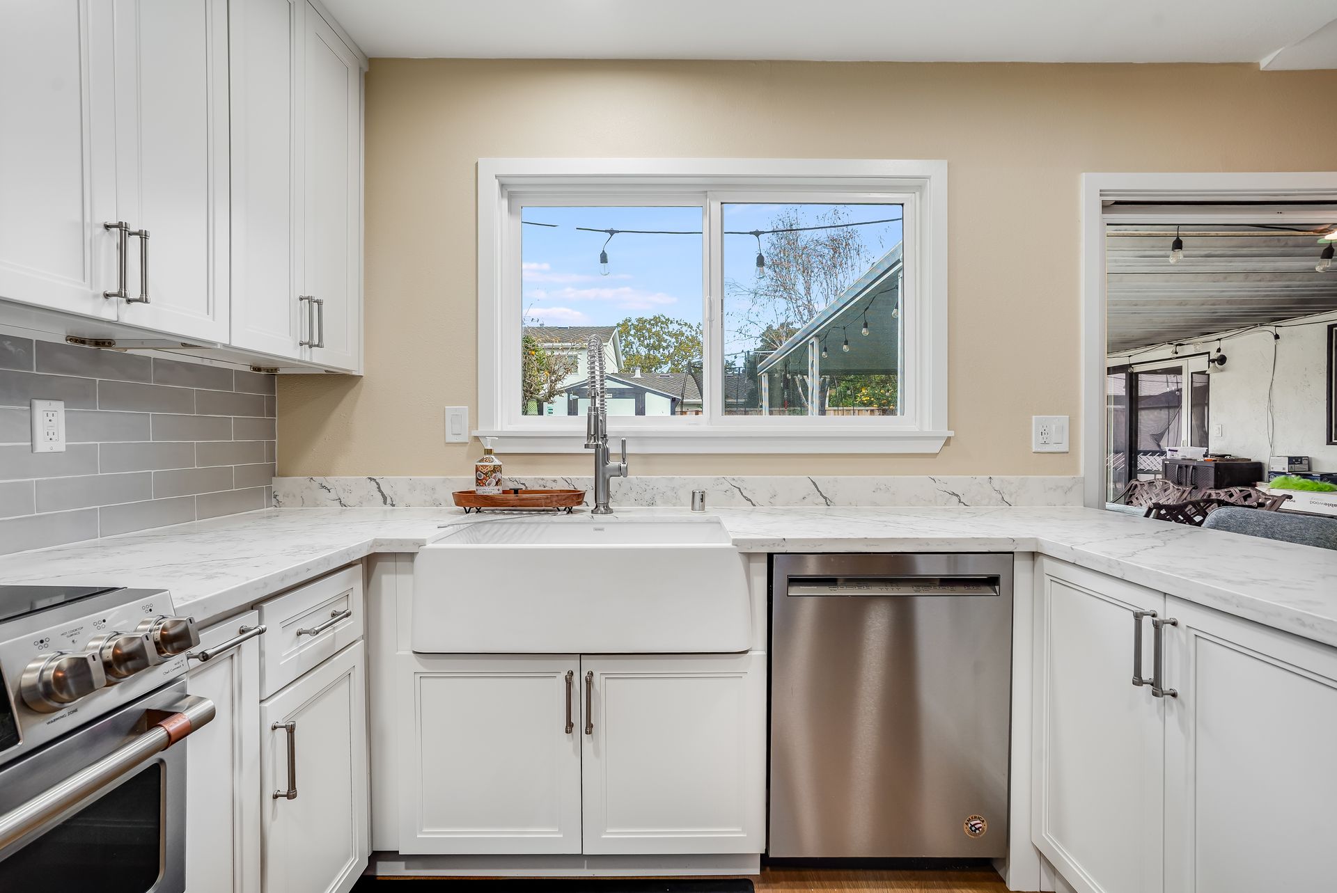 White kitchen with quartz countertops, stainless steel appliances, and a window with a view.