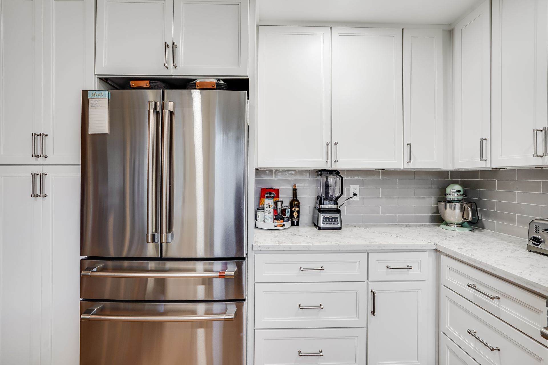 White kitchen with stainless steel refrigerator, white cabinets, and gray backsplash.