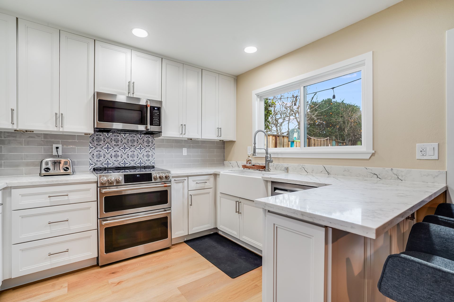 White kitchen with stainless steel appliances, light wood floors, and granite countertops.