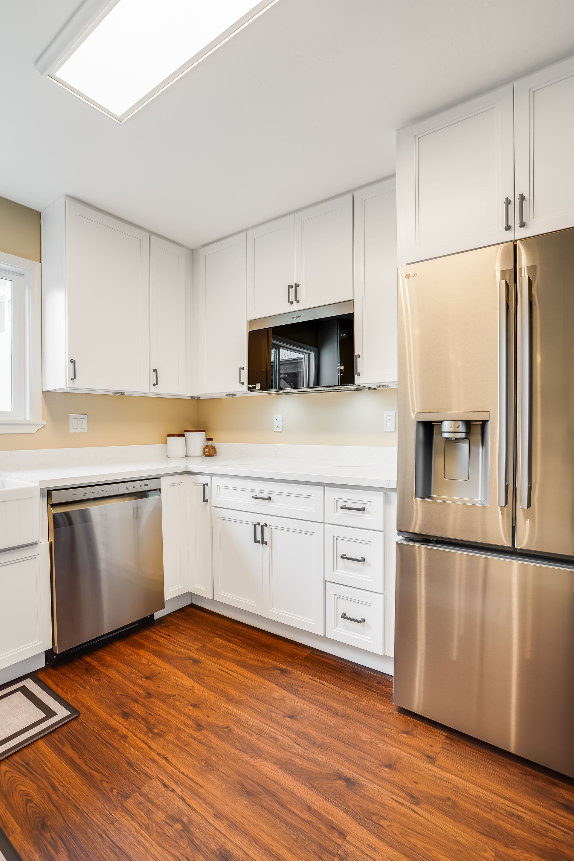Modern white kitchen with stainless steel appliances and wood floor.