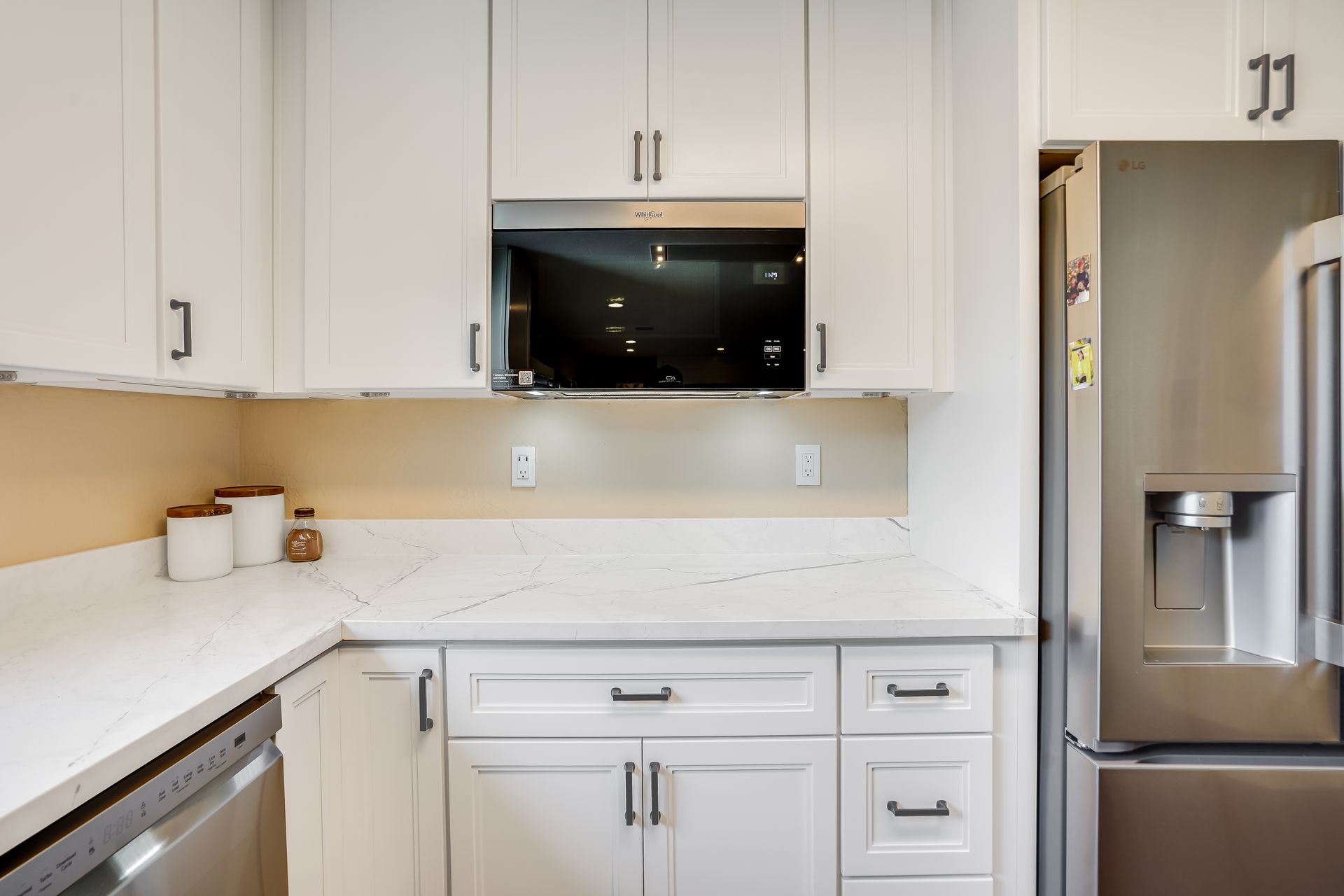 White kitchen with cabinets, microwave, countertop, and refrigerator.