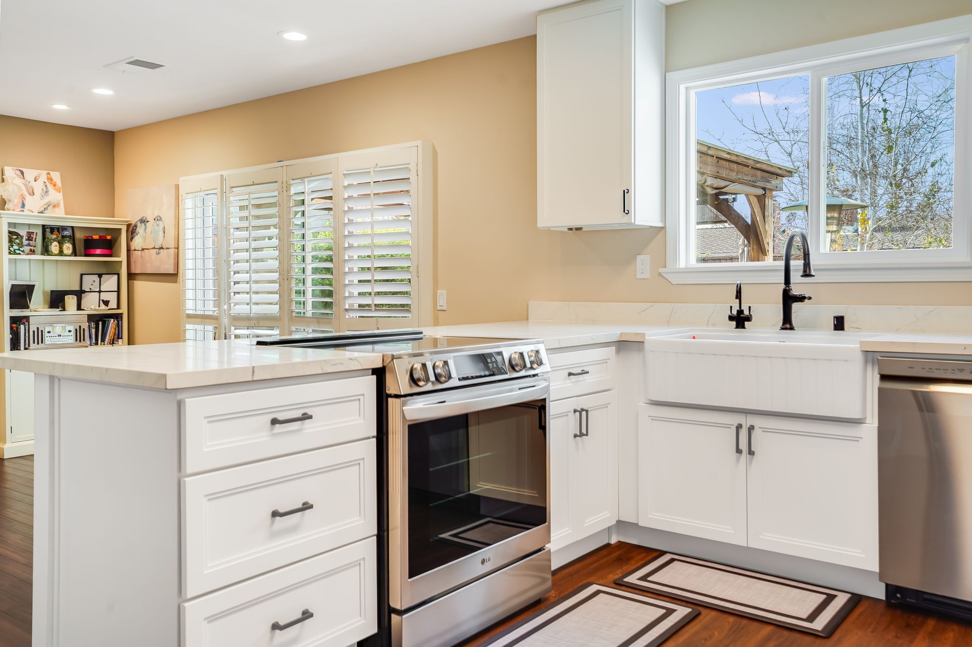 Bright white kitchen with stainless steel appliances, light countertops, and shutters on a window.