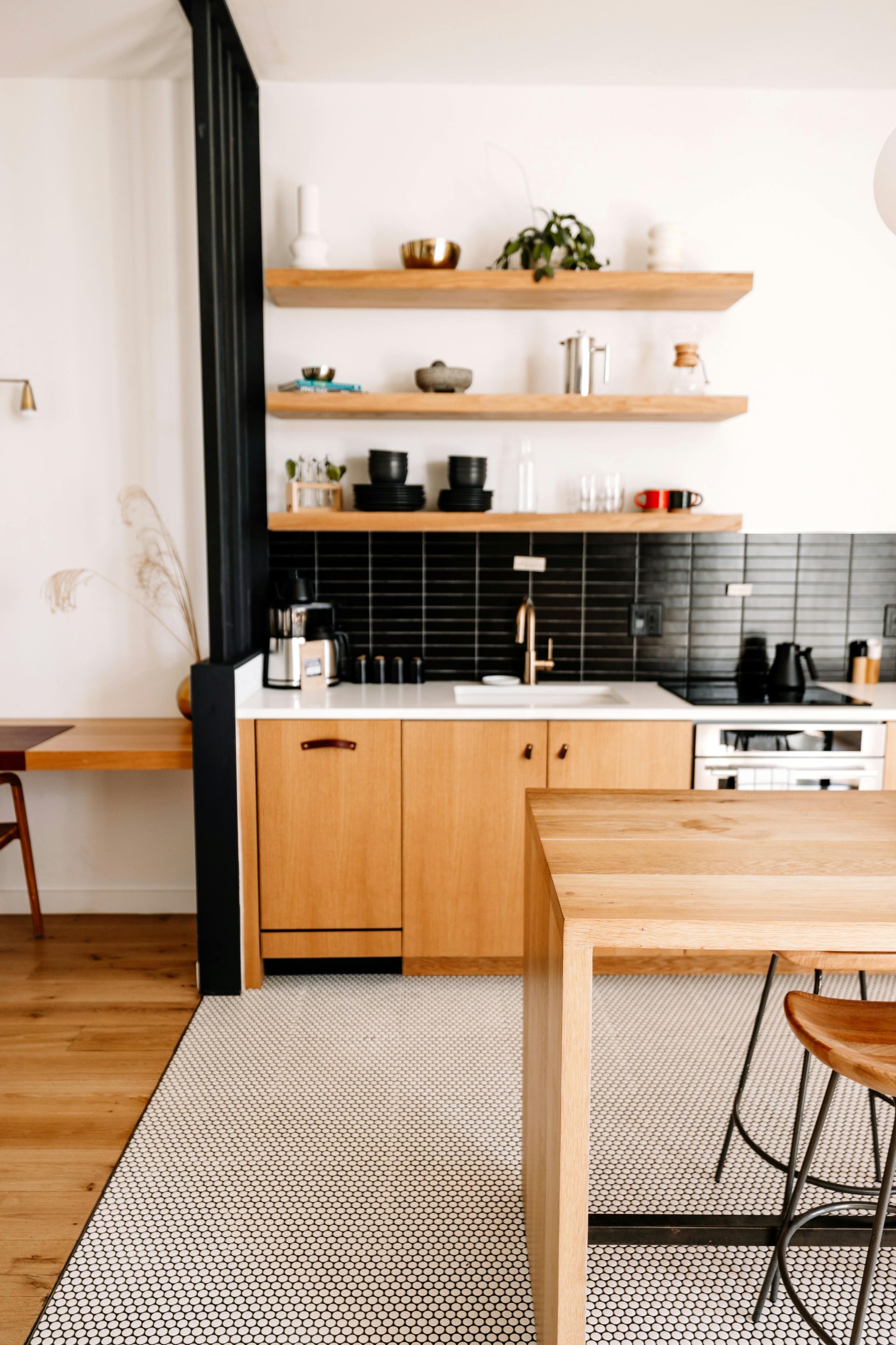 Kitchen area with light wood cabinets, black tile backsplash, open shelves, and a rug.
