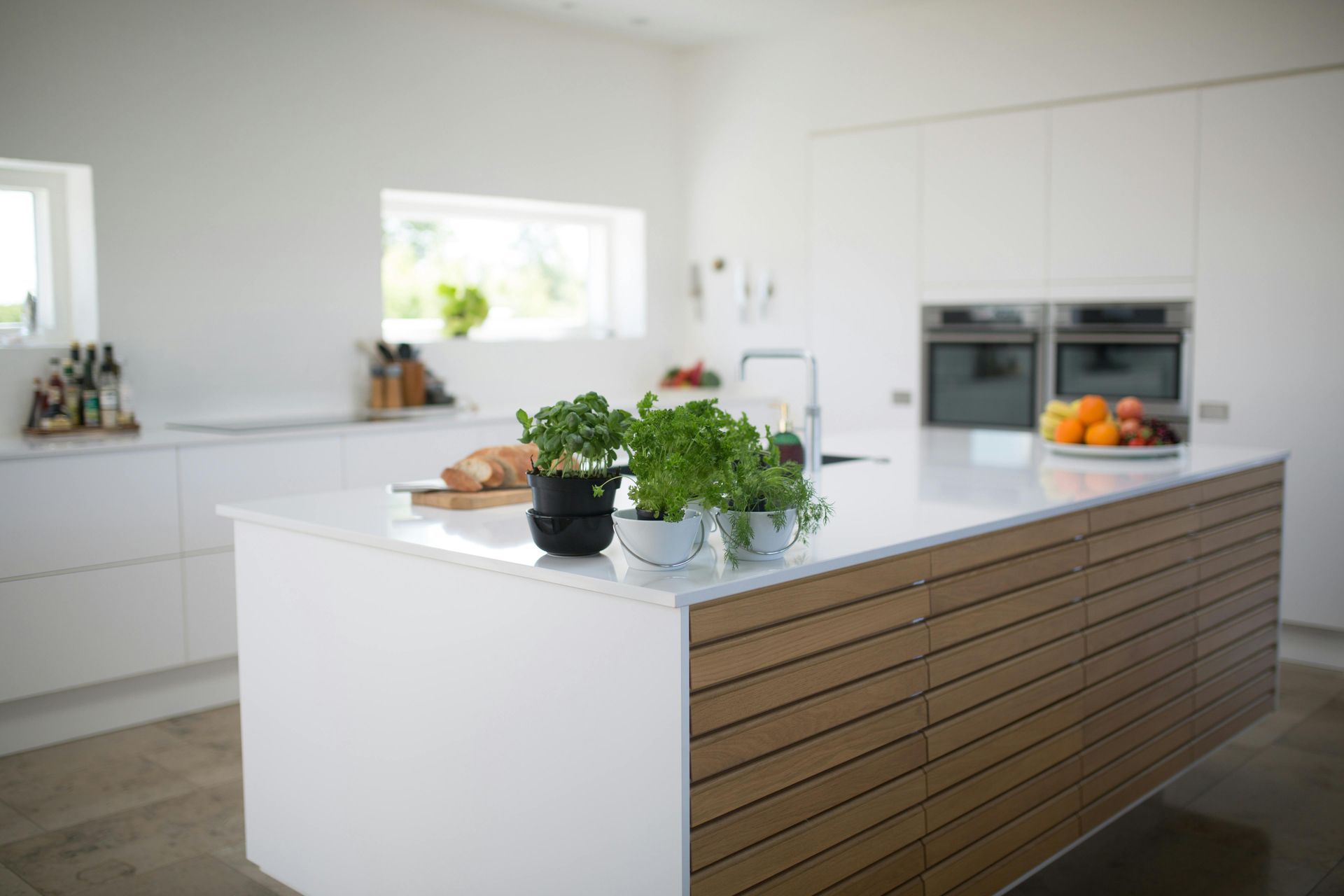 Modern white kitchen with a large island featuring herbs and a wood-slatted front.