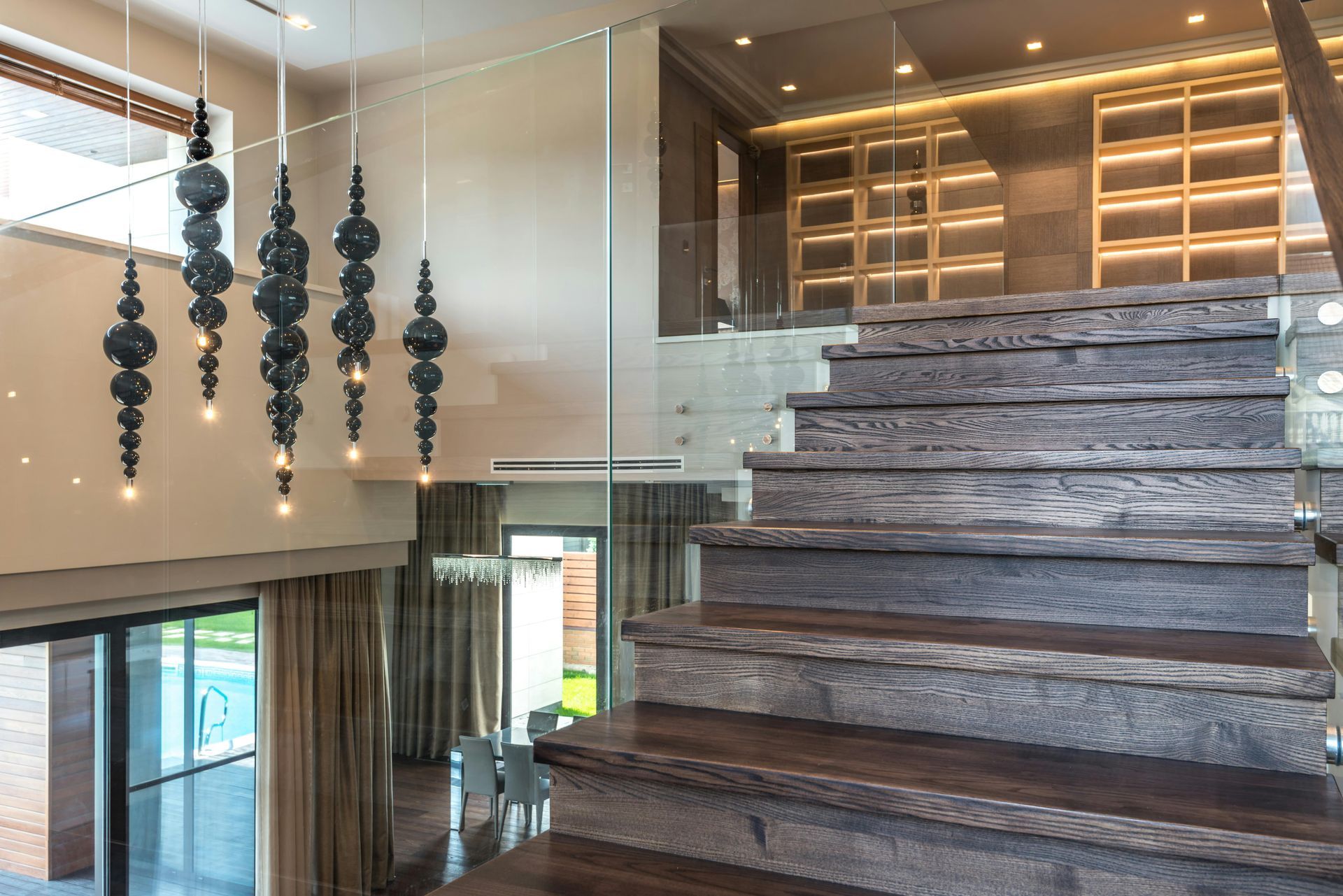 Wooden staircase leading upwards in a modern, open-concept home. Chandelier hangs from high ceiling.