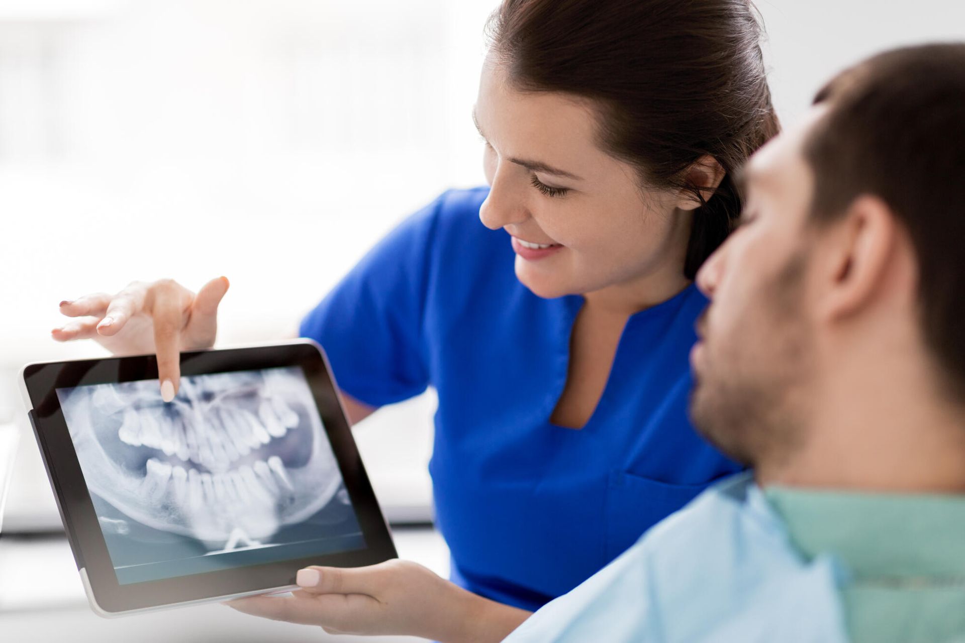 A dentist is showing a patient an x-ray of his teeth on a tablet.