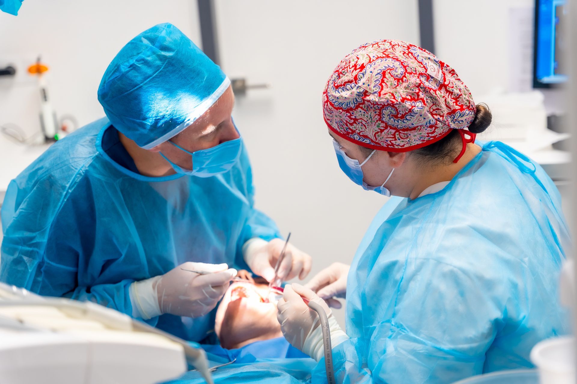 Two surgeons in blue scrubs operating on a patient in a dental clinic.