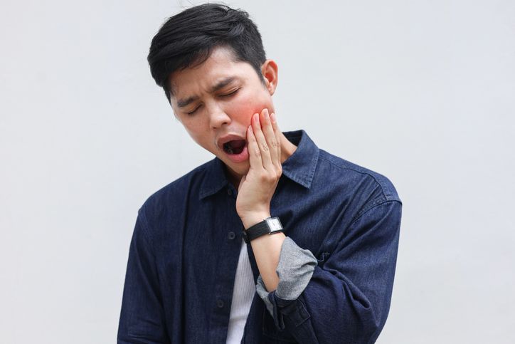 Man with hand on cheek, mouth open, showing discomfort, red cheek.