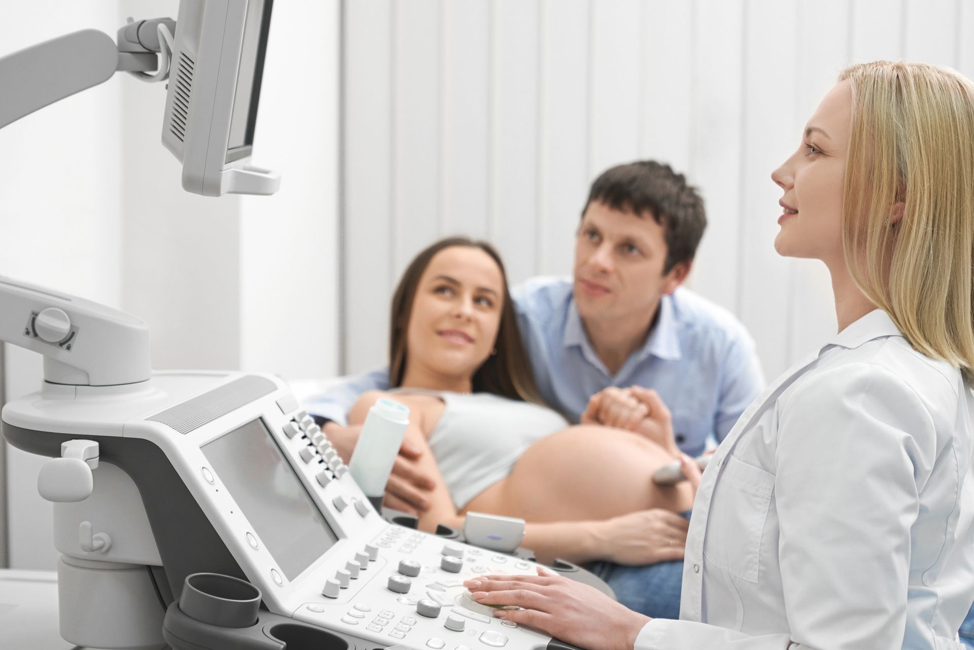 Pregnant woman and partner receive ultrasound scan in a clinic setting. Doctor operates the machine.