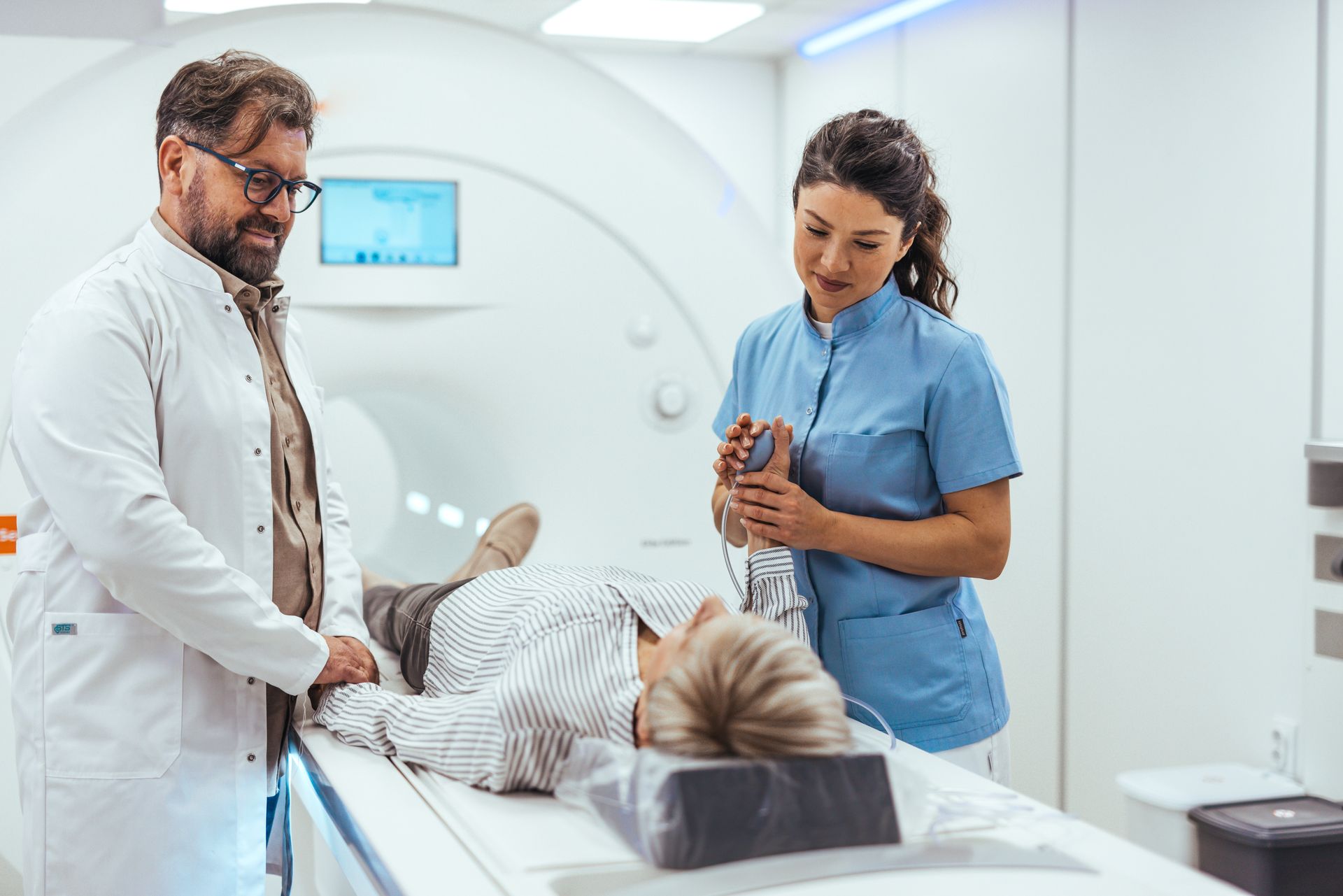 Doctor and nurse assisting a person during a CT scan. The patient lies on a table inside the machine.
