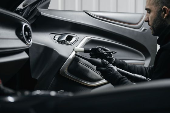 View of an Auto Detailing Worker Cleaning the Black Interior of Car With a Brush and a Small Vacuum View of an Auto Detailing Worker Cleaning the Black Interior of Car With a Brush and a Small Vacuum