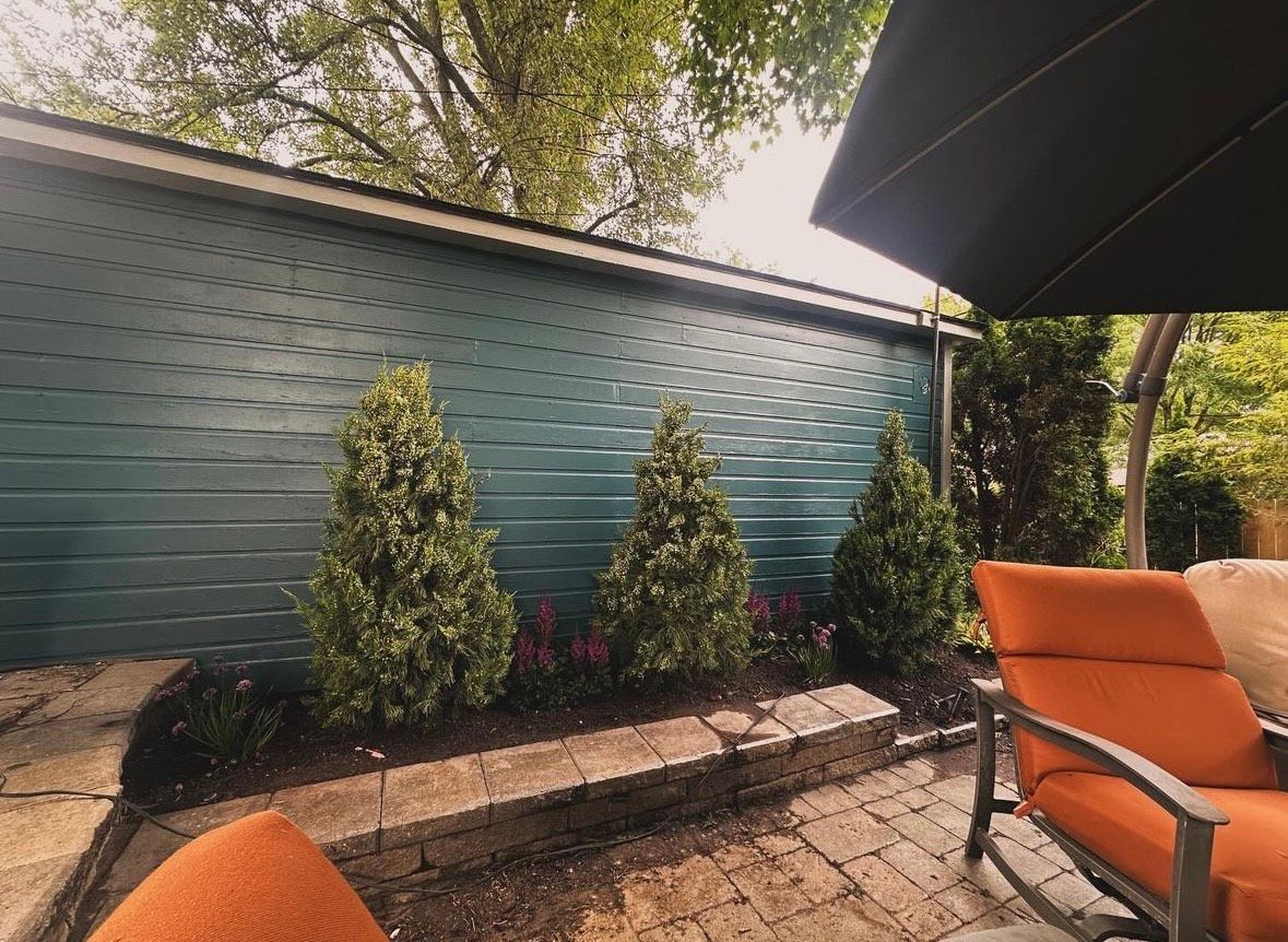 A patio with a couch , chair and umbrella in front of a blue wall.