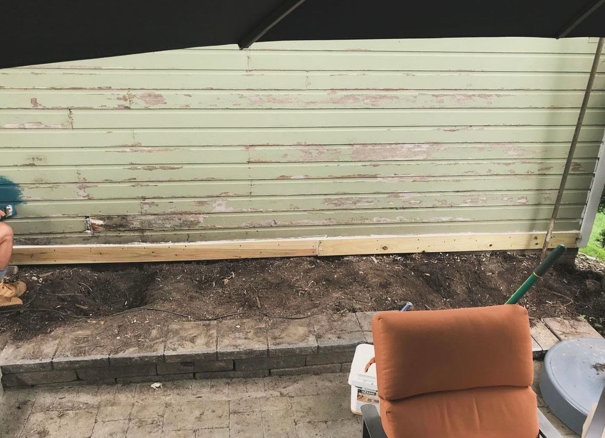 A patio with a chair and umbrella in front of a green wall.