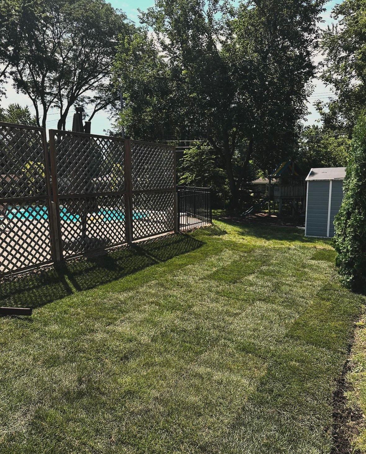 A backyard with a fence and a pool in the background.