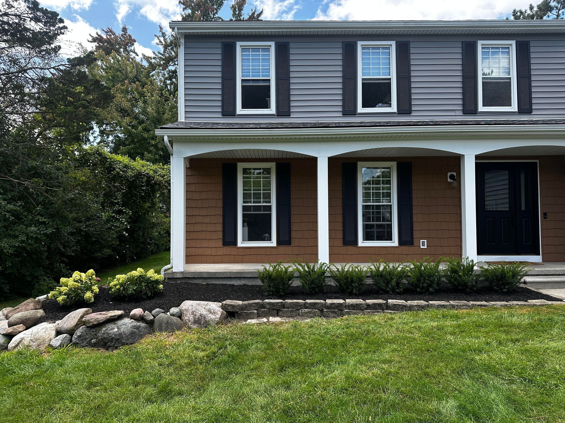 The front of a house with a large porch and black shutters.
