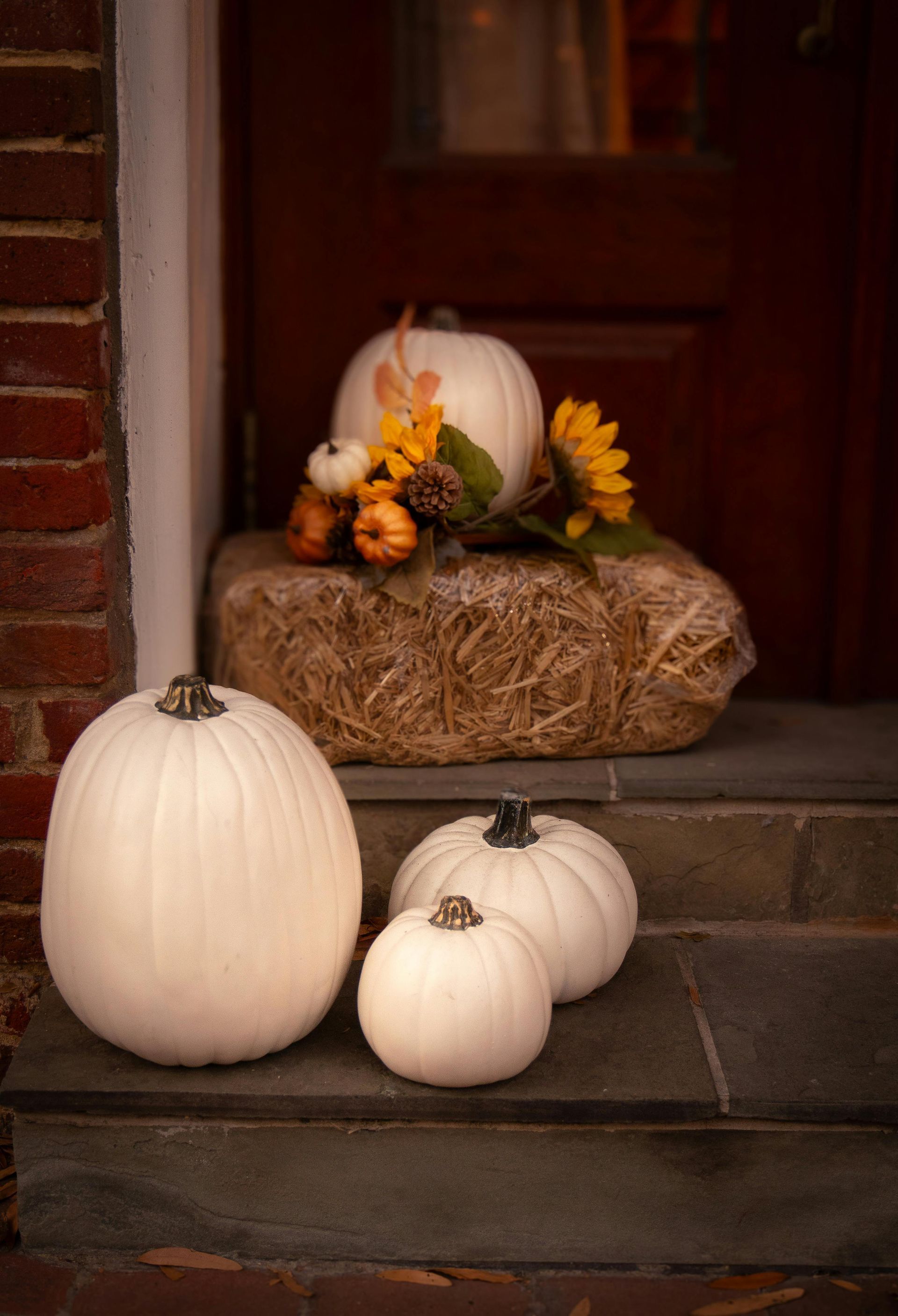 White pumpkins on a porch step with a hay bale and autumn decor.