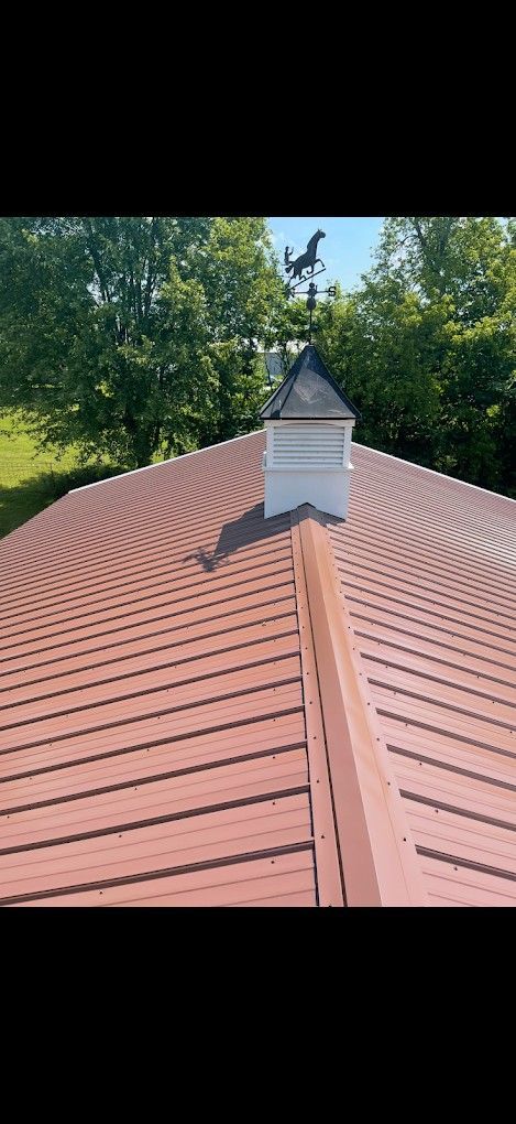 Red metal roof with a white cupola, surrounded by green trees under a blue sky