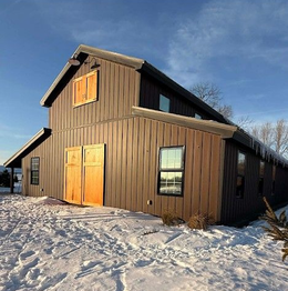 Brown barn-style building with orange doors on a snowy lot under a blue sky