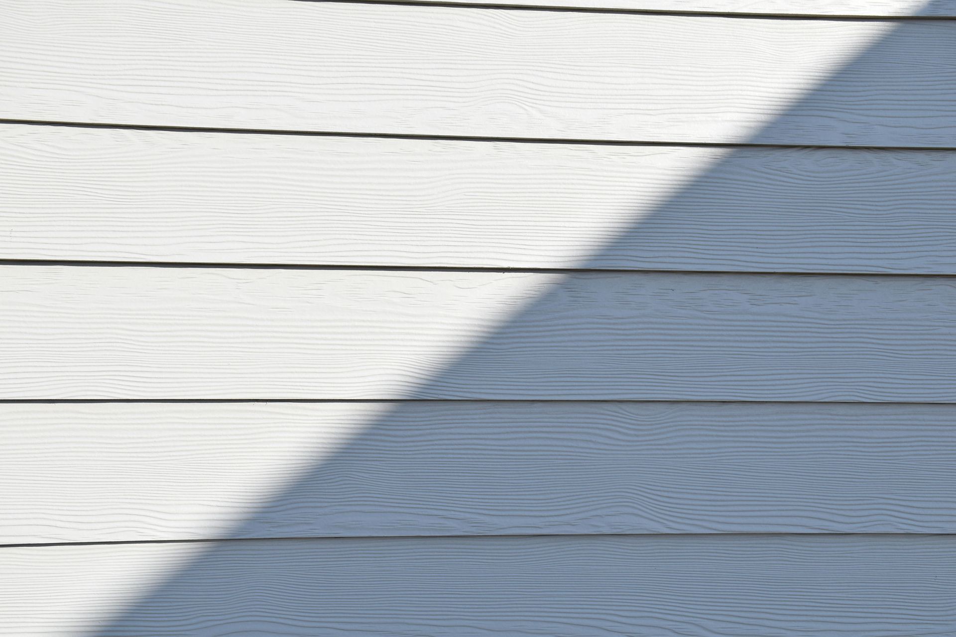 White horizontal wooden siding with a large diagonal shadow across it.