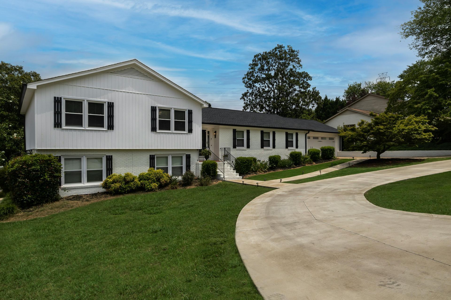 White suburban house with a curved driveway, green lawn, and trees under a blue sky