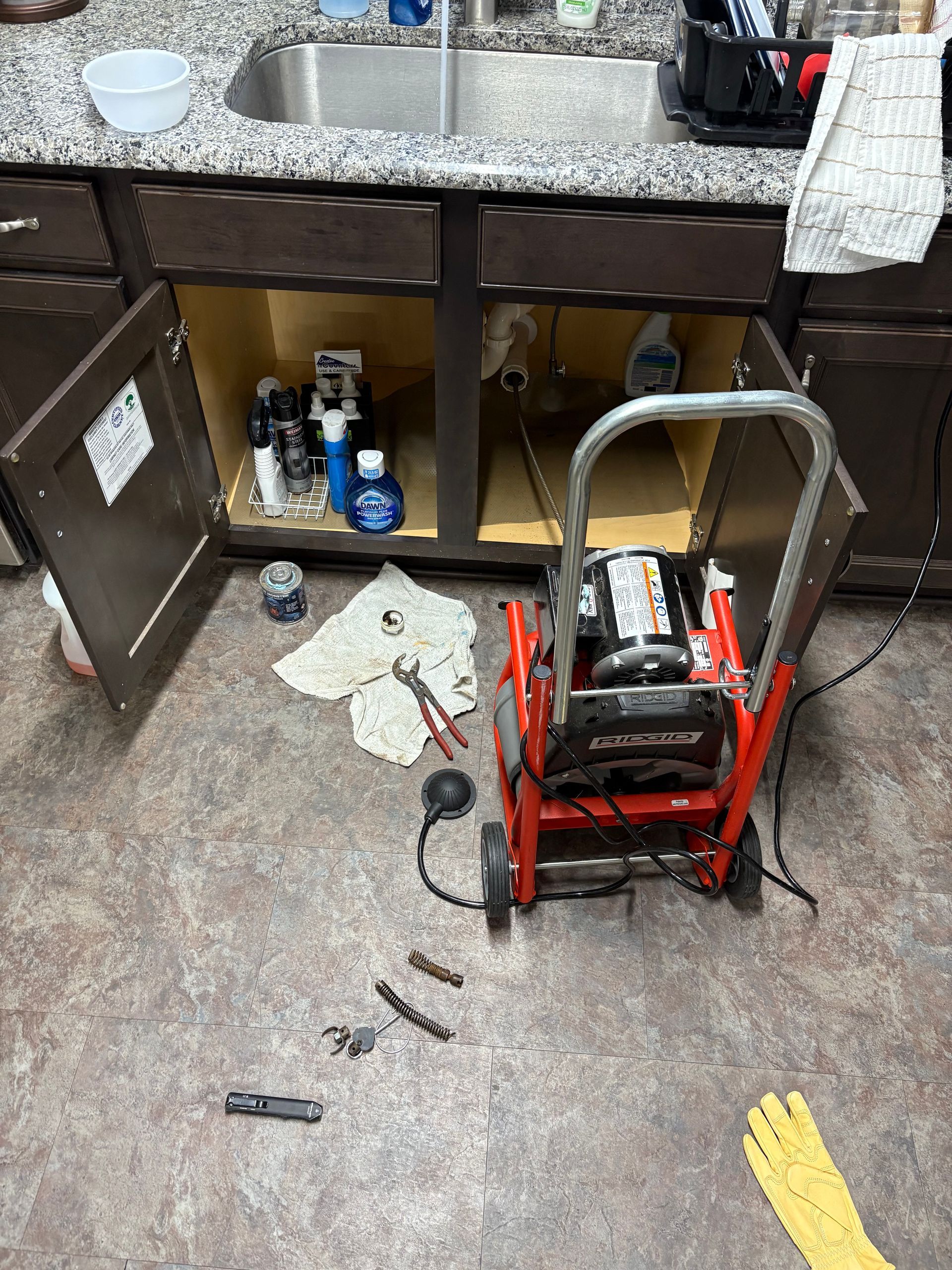 Plumber in blue overalls working on a sink faucet in a bathroom.
