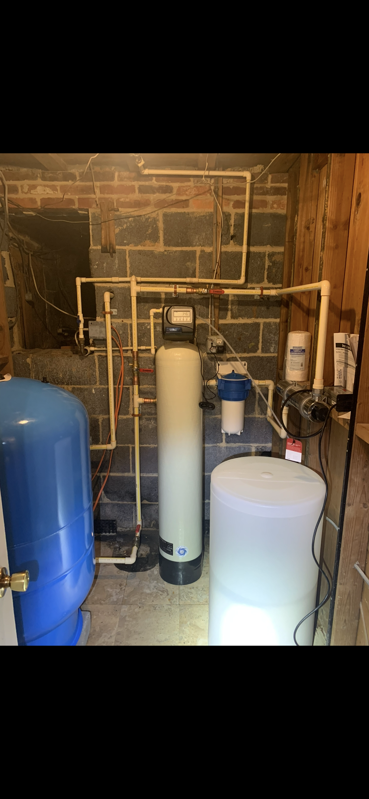 Plumber in blue uniform, using a multimeter on a water heater in a utility room.