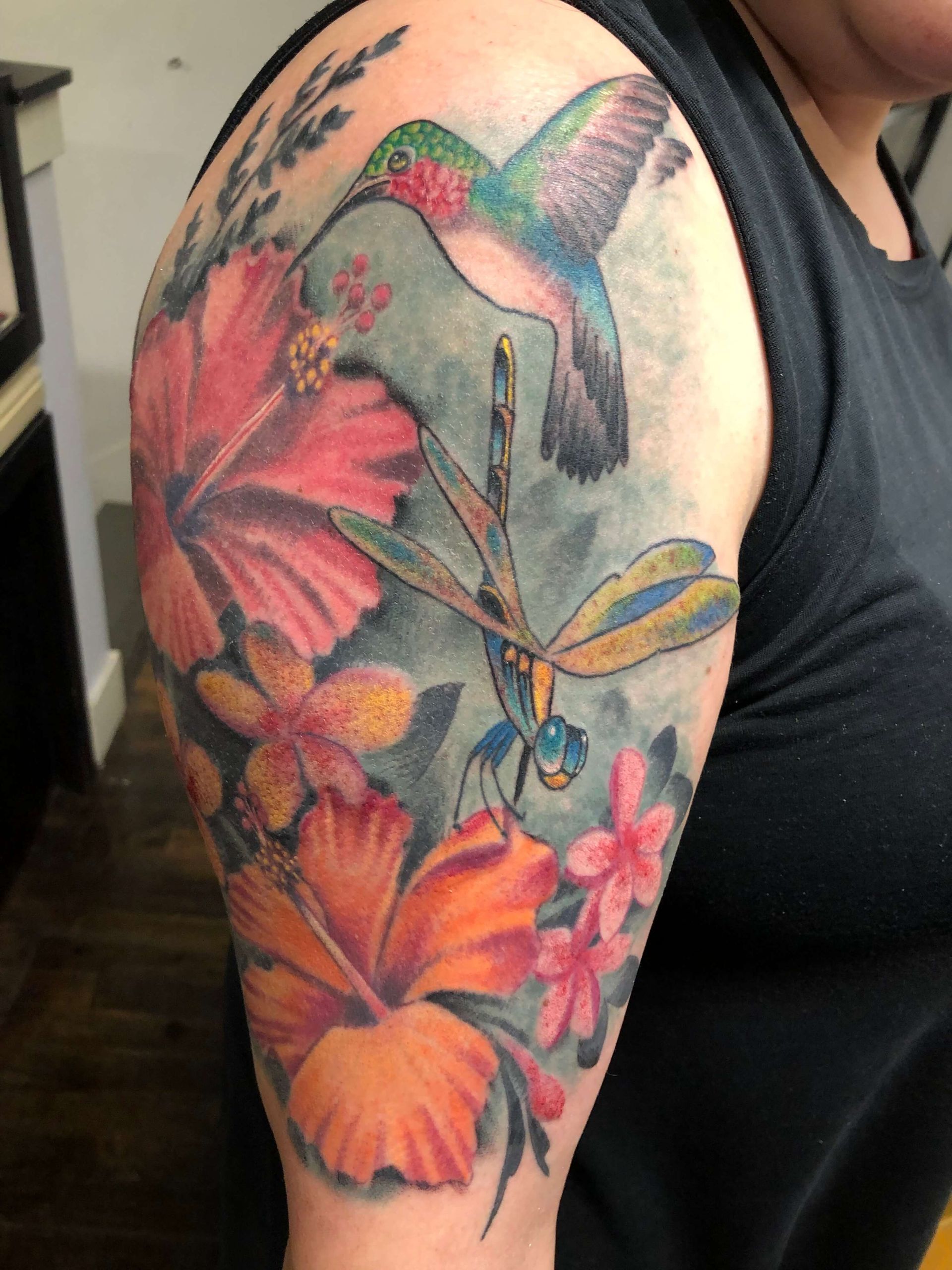 A woman has a tattoo of a hummingbird and dragonfly on her arm
