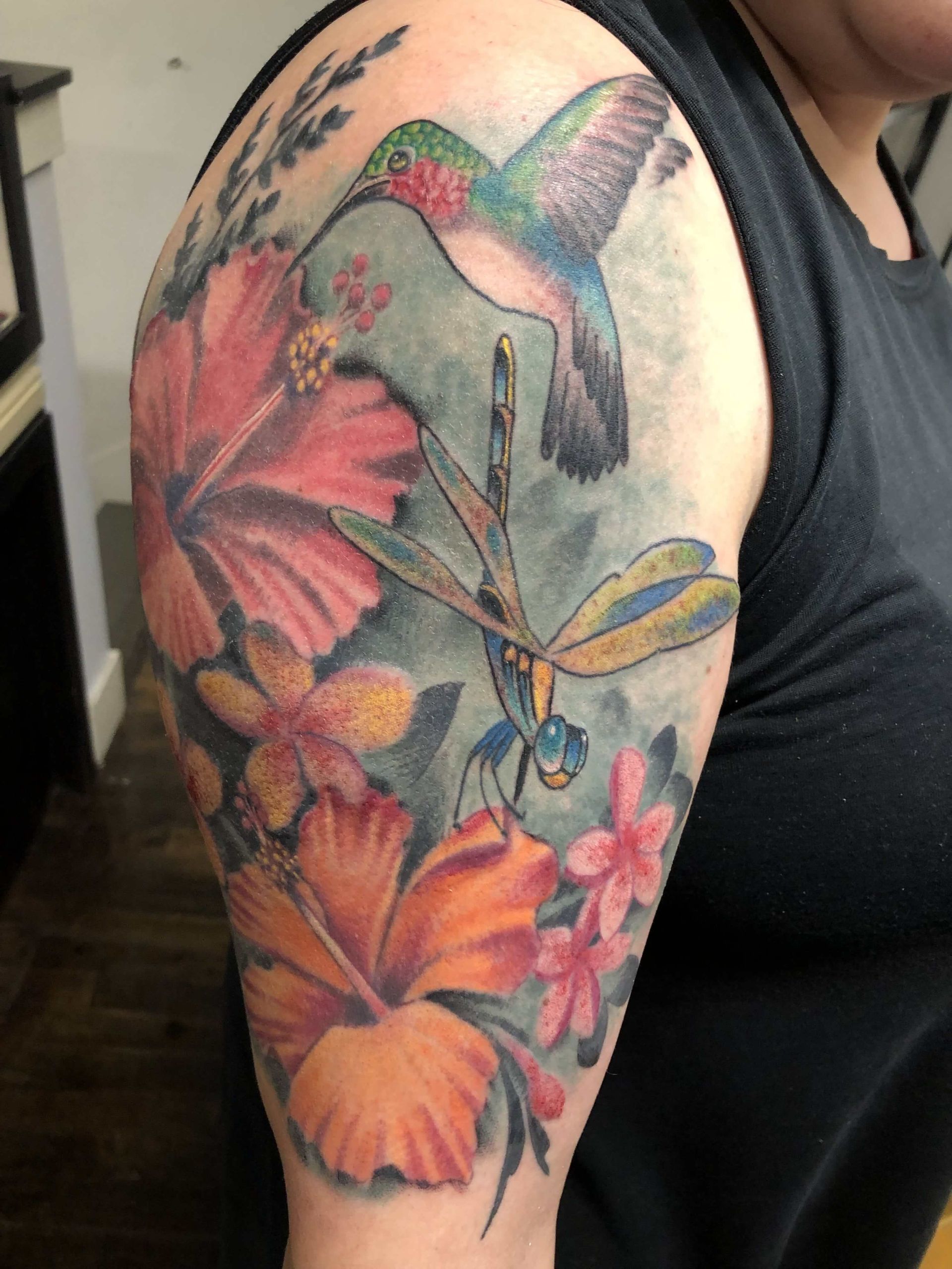 A woman has a tattoo of a hummingbird and dragonfly on her arm