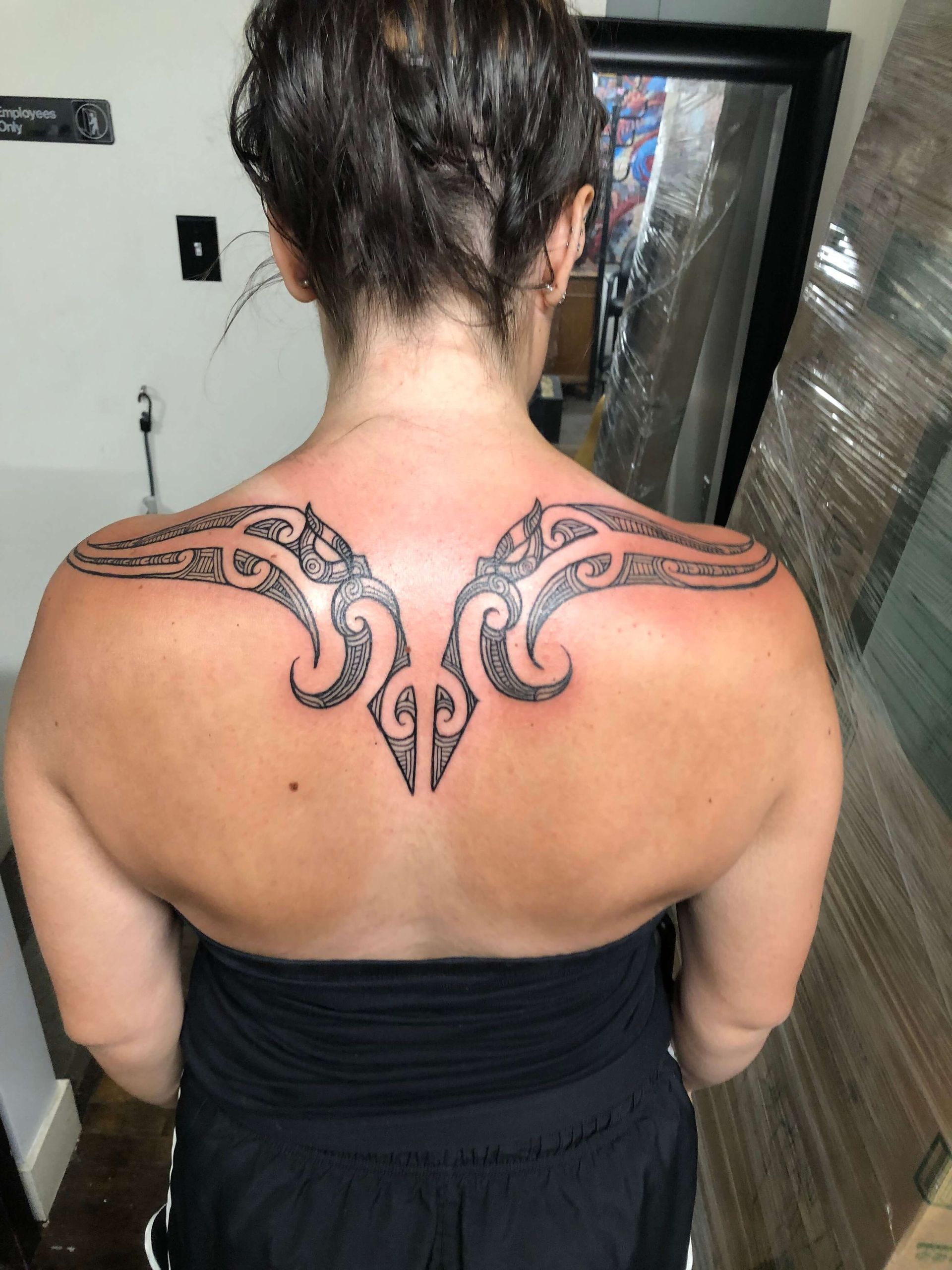 A woman has a tattoo on her back and shoulder.
