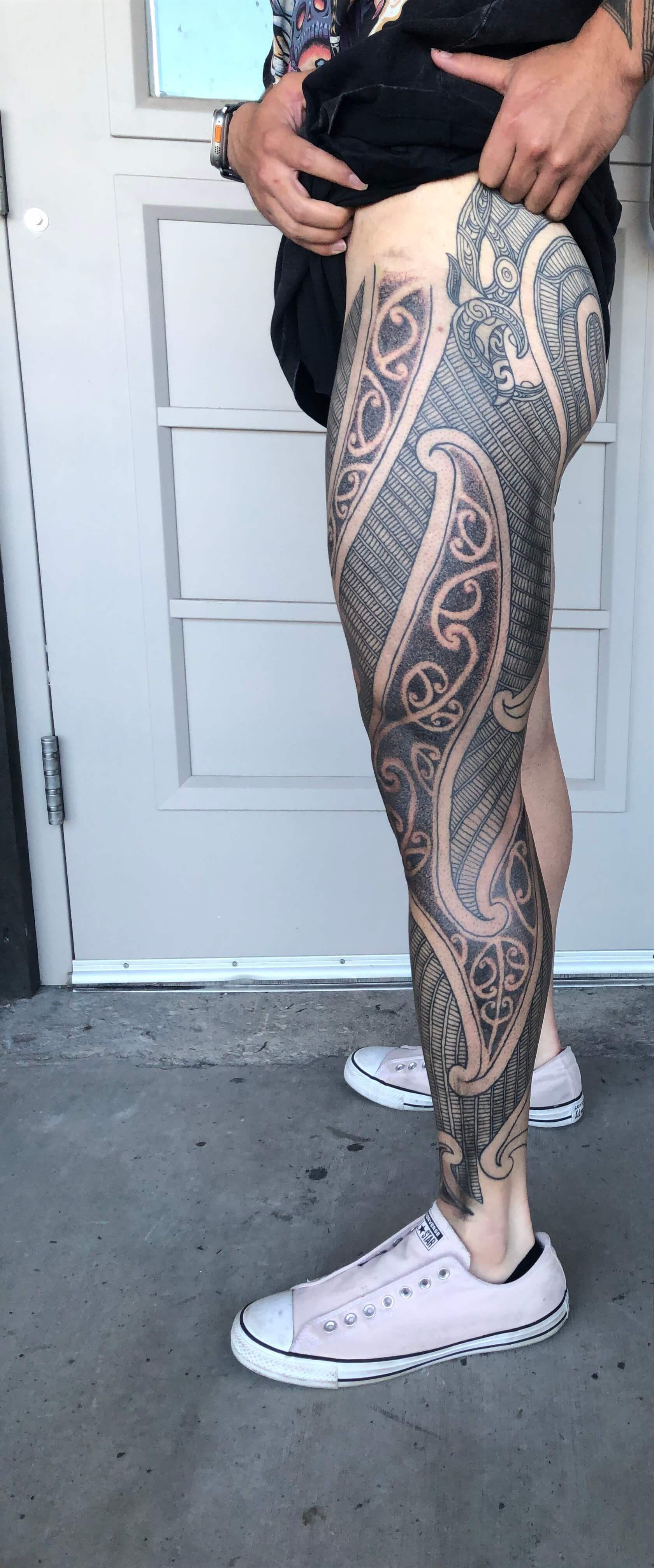 A woman with a tattoo on her leg is standing in front of a door.