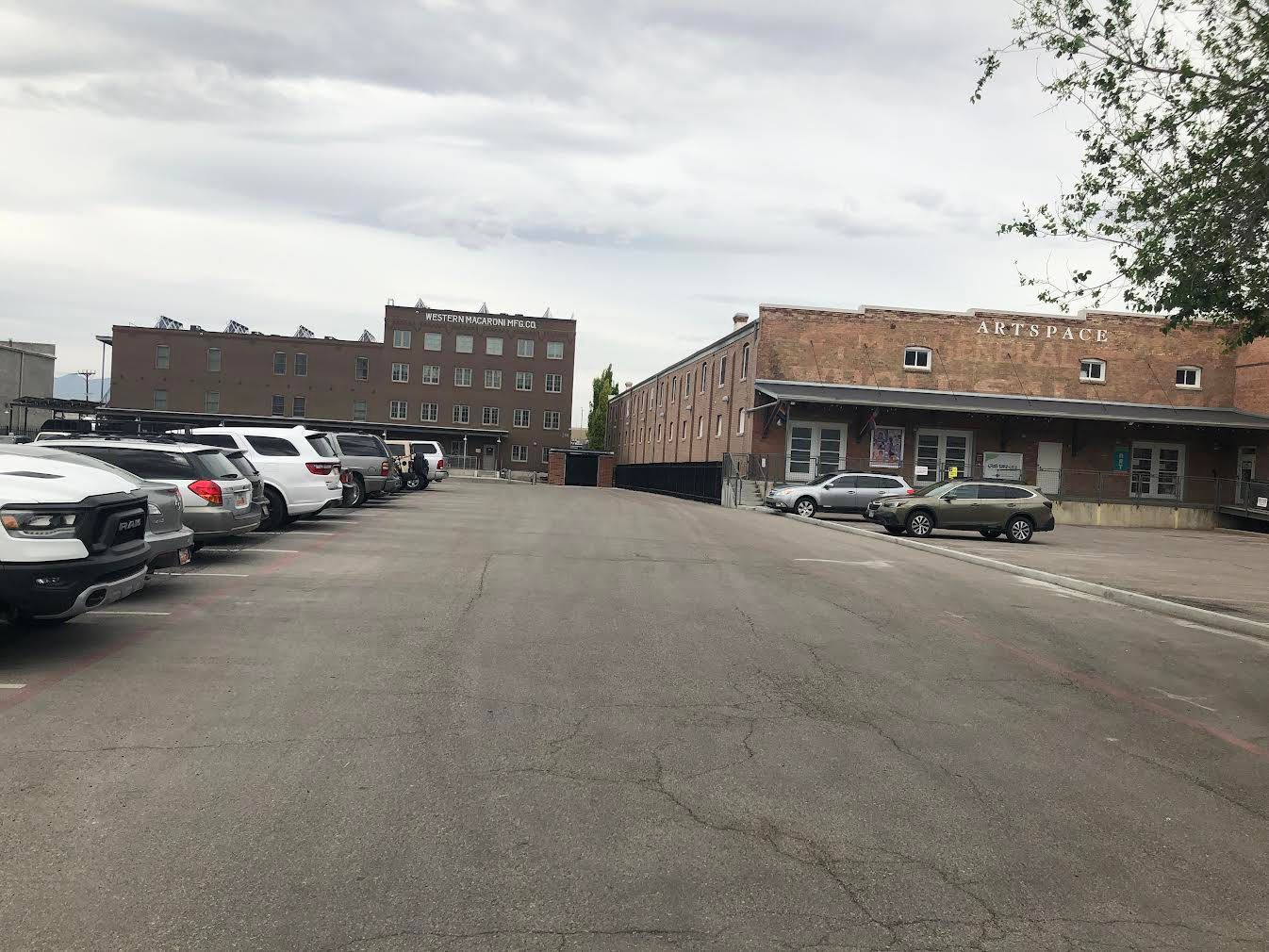 Parking lot with cars, brick buildings, and a cloudy sky.