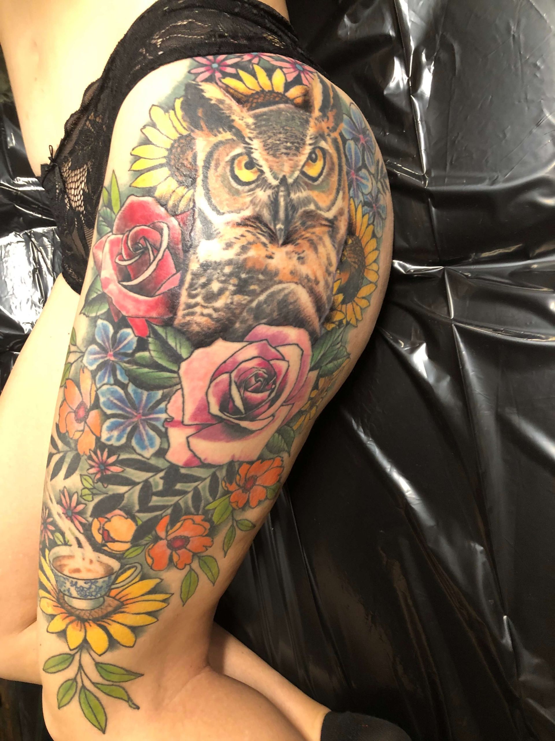 A woman has a tattoo of an owl and flowers on her leg
