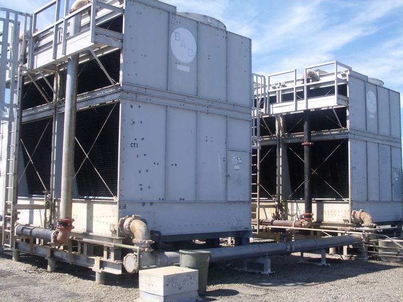 Two large, gray industrial cooling towers outdoors on a sunny day.