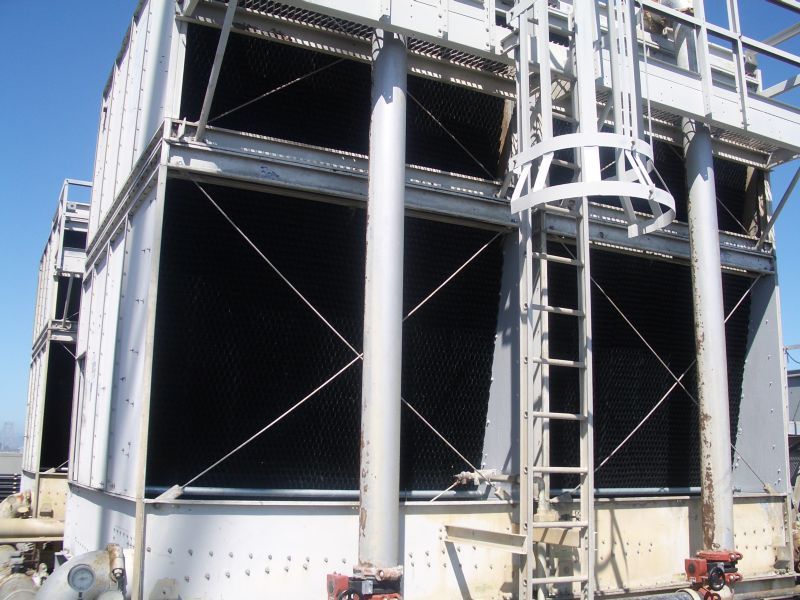 Cooling tower with metal frame, open grates, and access ladder against a blue sky.