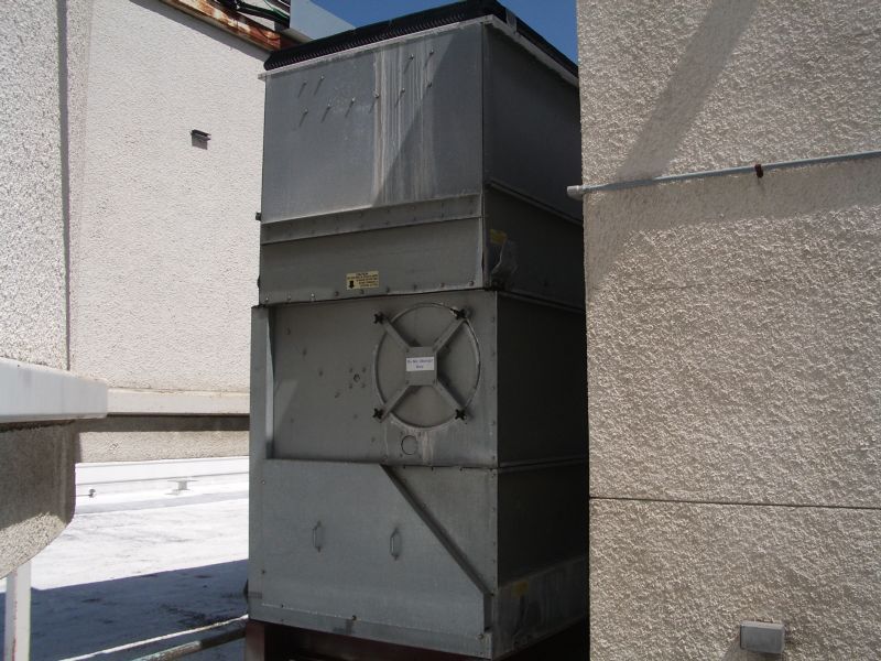 Large, gray HVAC unit on a building rooftop, positioned between two walls, under a sunny sky.