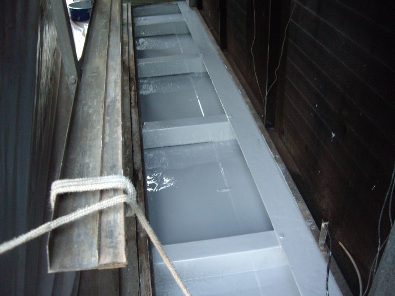 Interior view of a boat, showing painted grey sections. Wooden sides and a rope are visible.