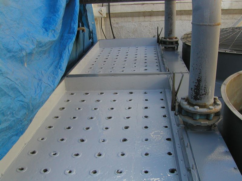 Gray metal industrial trough with evenly spaced holes, pipes, and a blue tarp.