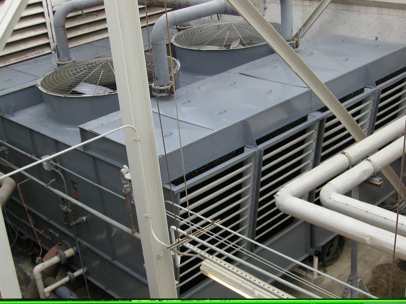 Large industrial cooling tower, gray metal, with ventilation louvers and pipes, outdoors.