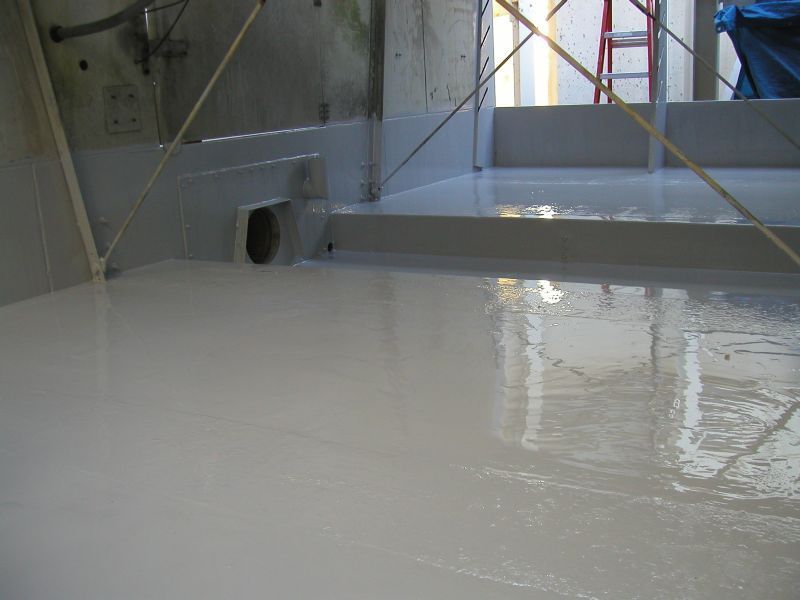 Gray coated interior with a drain. Reflective, wet surface, industrial setting.