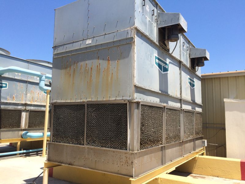 Large industrial cooling tower unit on a rooftop, weathered metal, blue sky.
