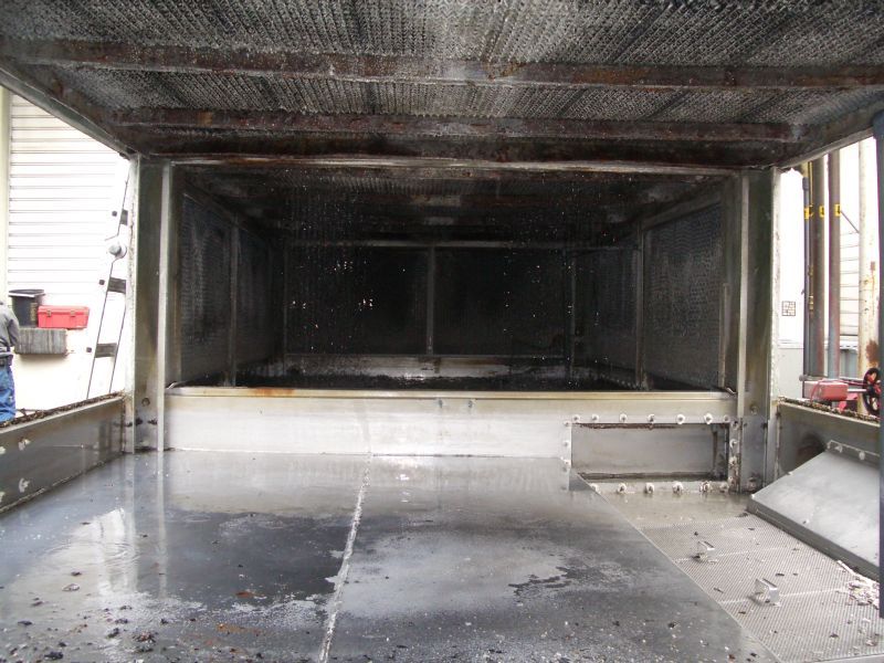 Inside of a large industrial metal enclosure, possibly a processing unit, with dark residue and a wet floor.