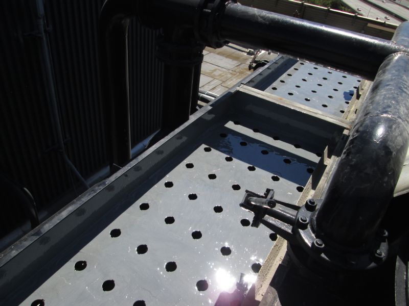 Overhead view of a metal platform with holes, pipes, and machinery against a building.