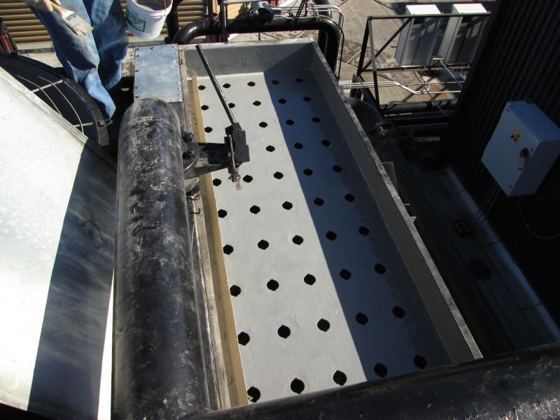 Rectangular metal tray with evenly spaced holes, possibly for filtration, on industrial equipment.