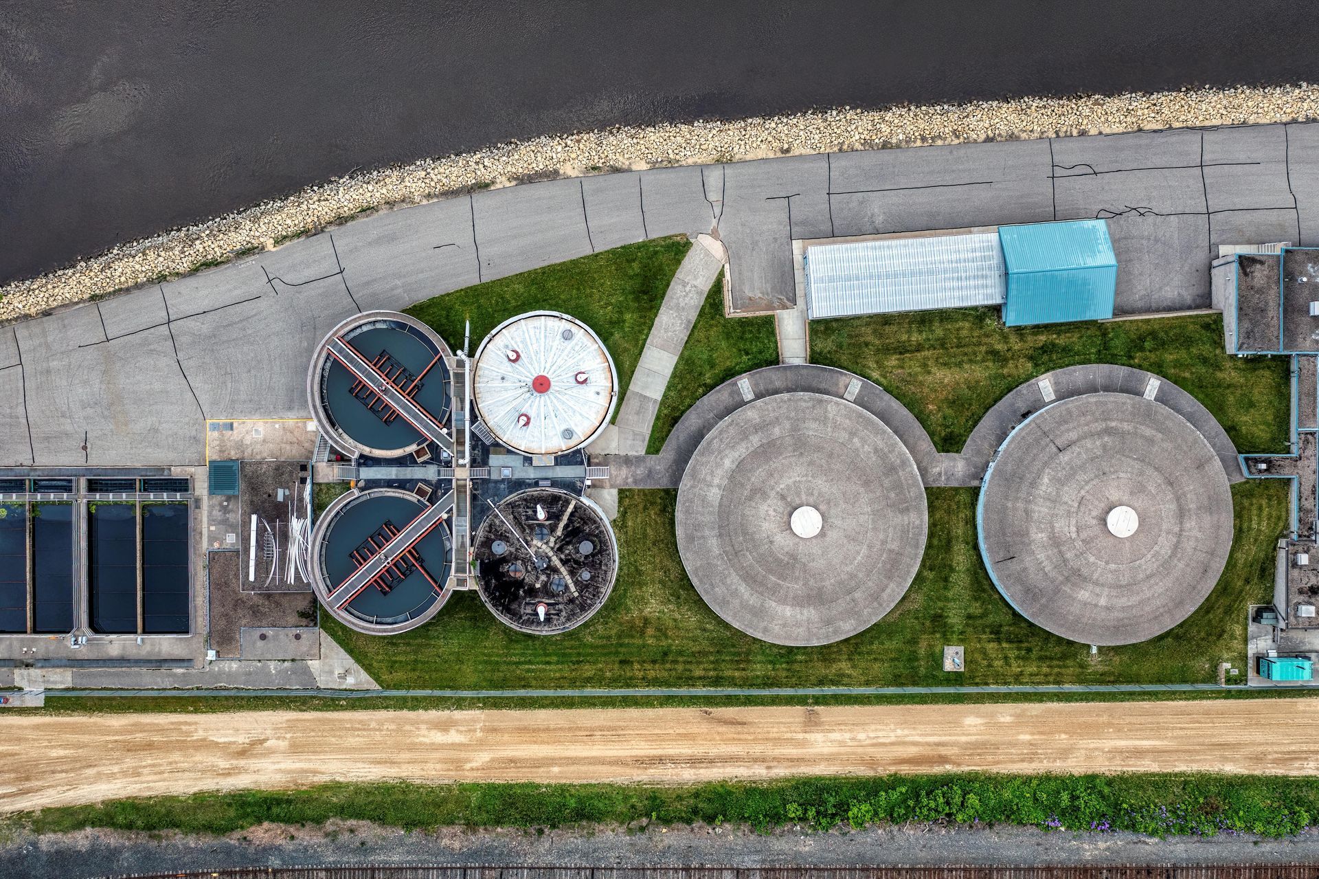 Aerial view of a wastewater treatment plant with several circular tanks and buildings along a waterway.