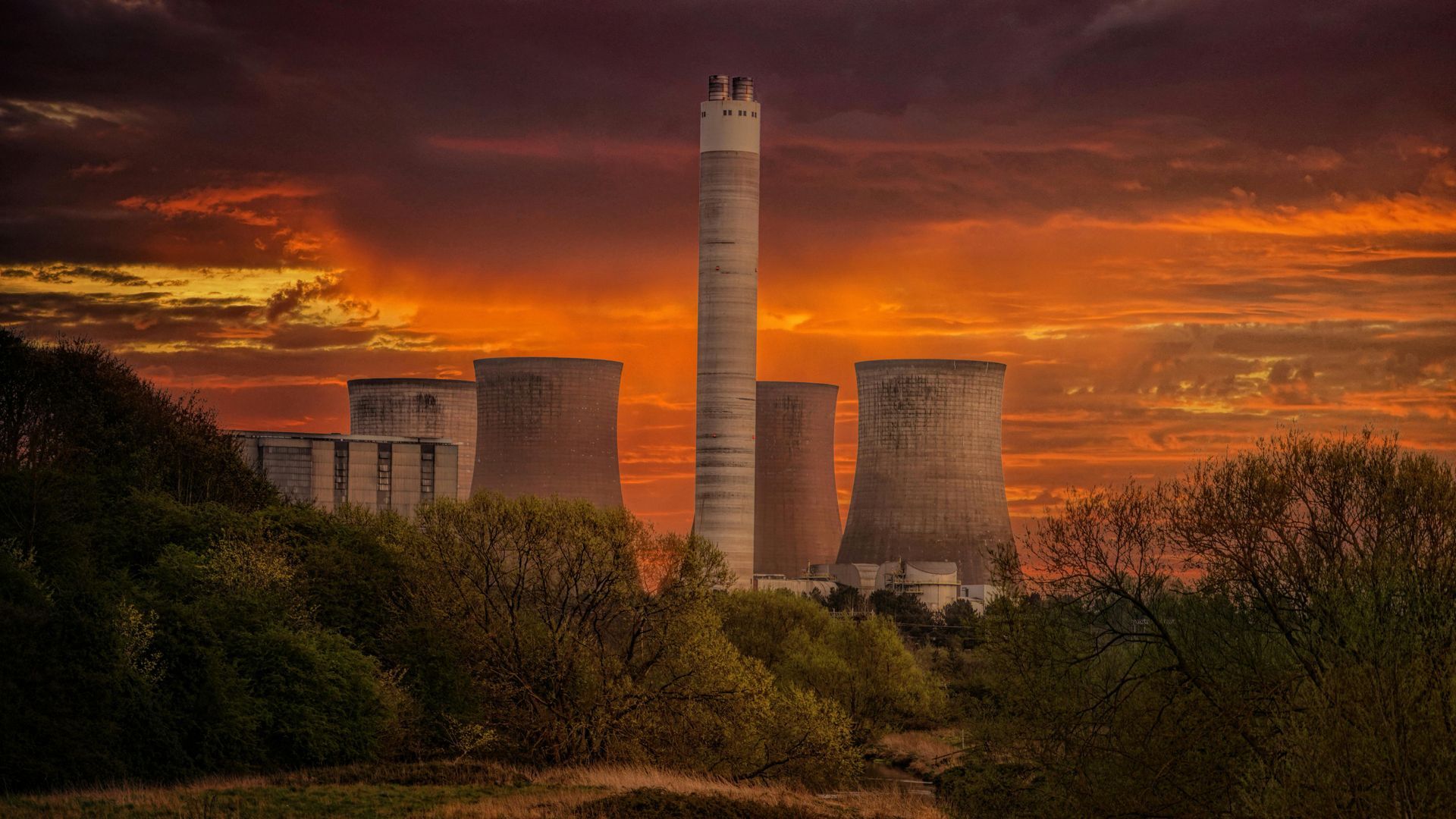 Power plant chimneys against a fiery sunset sky.