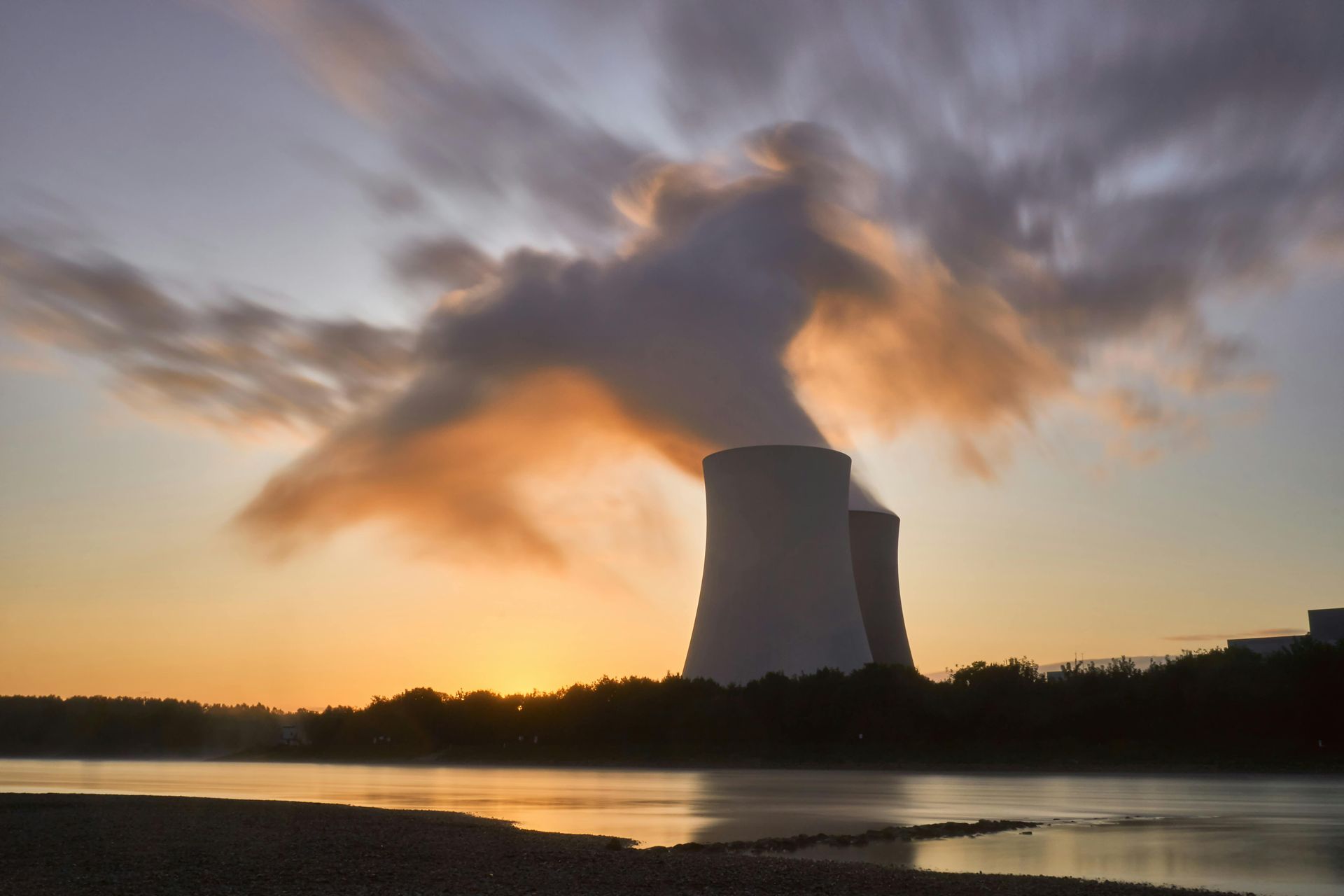 Nuclear power plant with cooling towers, emitting steam against a sunset sky.