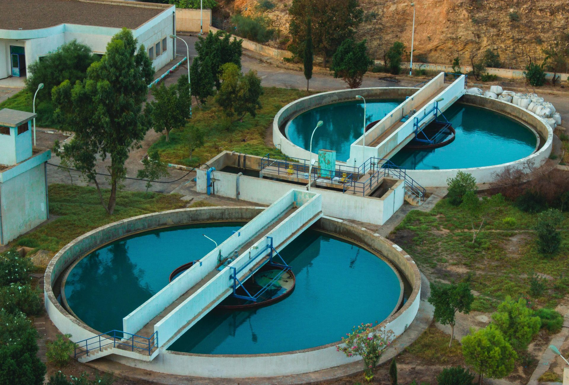 Aerial view of a wastewater treatment plant with two large circular tanks, blue water, and white structures.