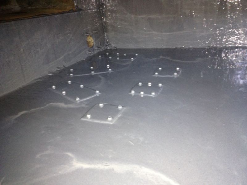 Interior of a dark, wet space with several square, bolted metal plates embedded in a gray surface.