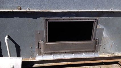 Metal frame with a rectangular opening, likely for ventilation, set in a larger metal structure.