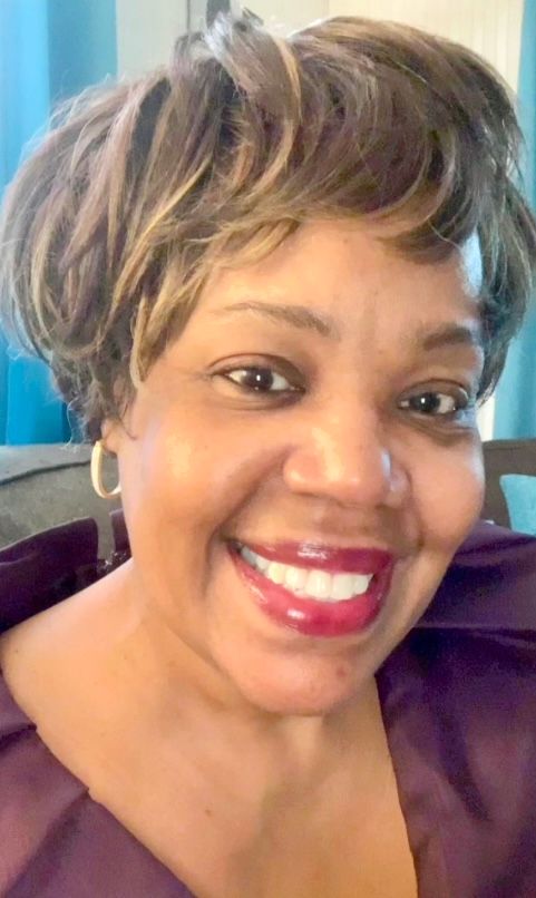 A woman is sitting at a desk with a laptop and a vase of flowers.